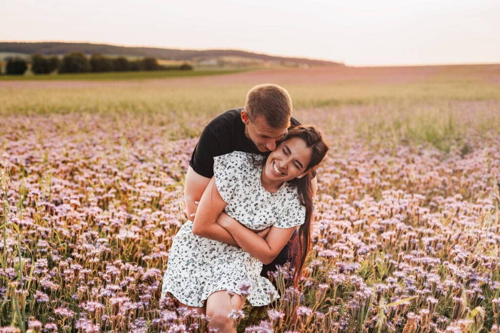 Romantická fotokrese na louce s květinami, šťastný pár, letní focení, přírodní portrét, spojující lásku a krásu krajiny.