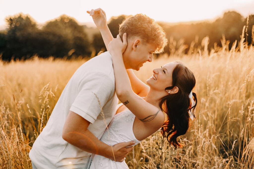 Láskyplný moment mezi milujícími se pár v zlaté hodinu na louce během západu slunce, ideální pro romantické a svatební fotografie.