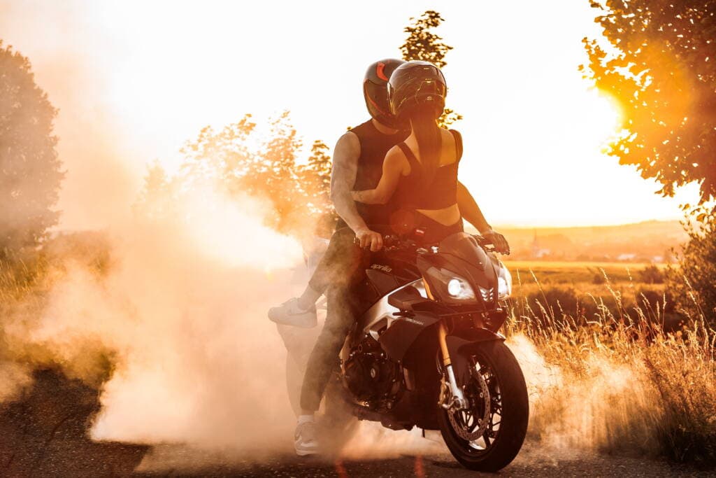 Osobní motocyklista s ženou na stroji při západu slunce, adrenalinová jízda na sportovním motocyklu, dynamická akční scéna, letní outdoorové focení, cestování motorověmě motocyklem, moto zábava a adrenalin.